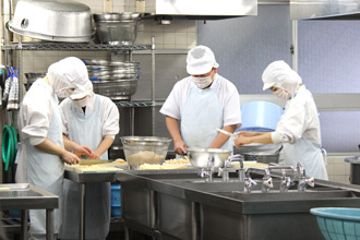 学校調理室内で指導する奥田さん（写真中央）